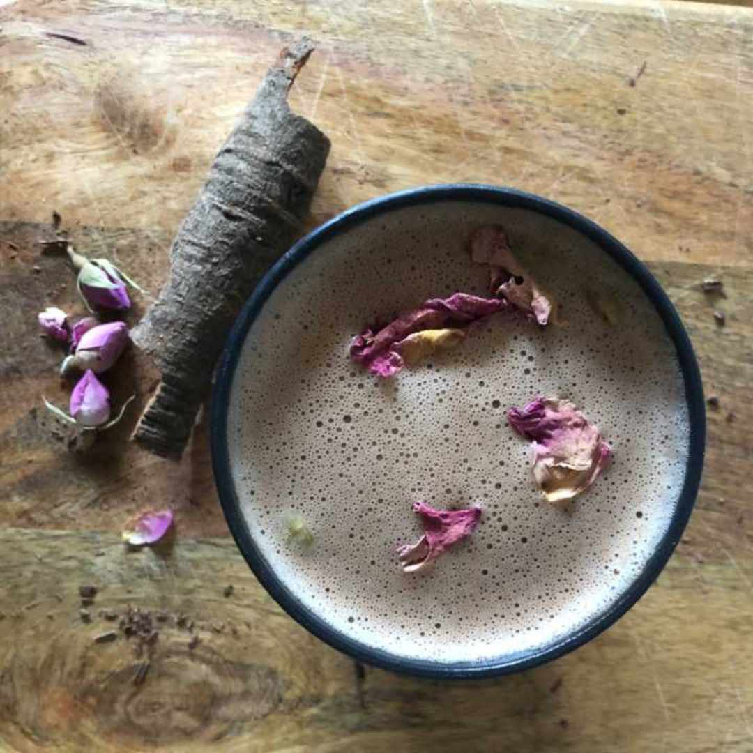 A beautiful cup of hot chocolate with rose petals and cinnamon on a wooden board