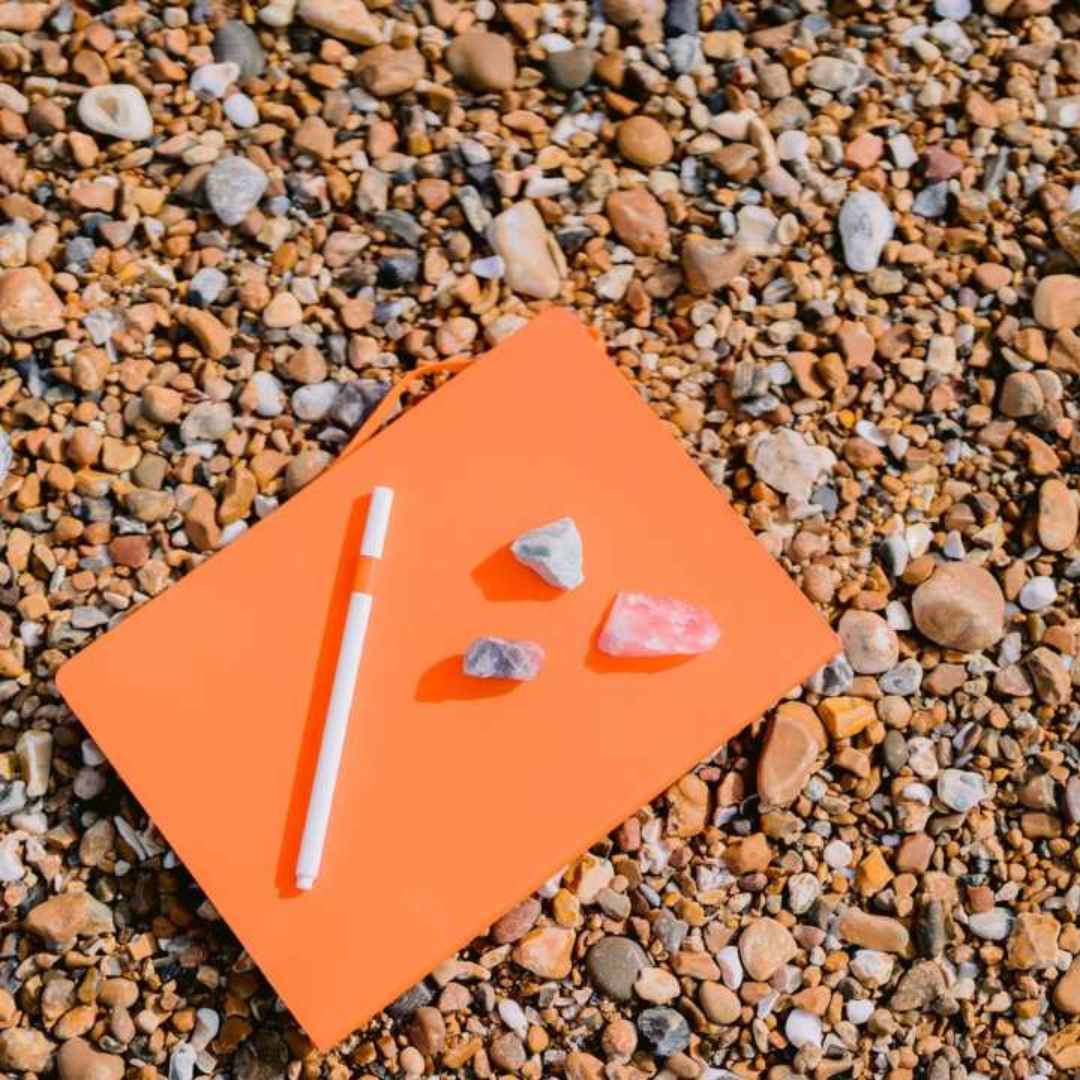 Orange notebeook on a beach with a pen and with crystals