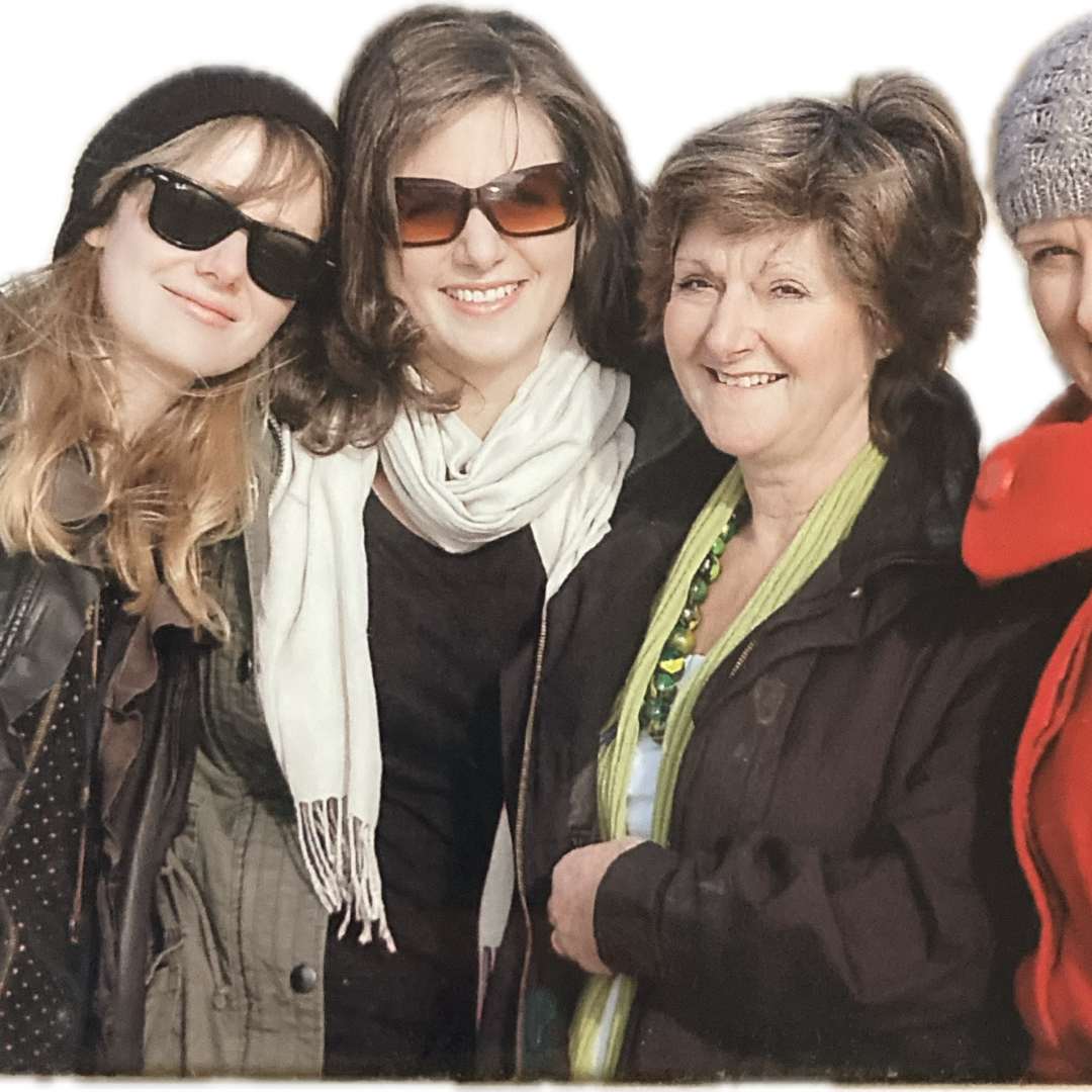 4 women smiling at the camera. all are white and two have dark glasses on.