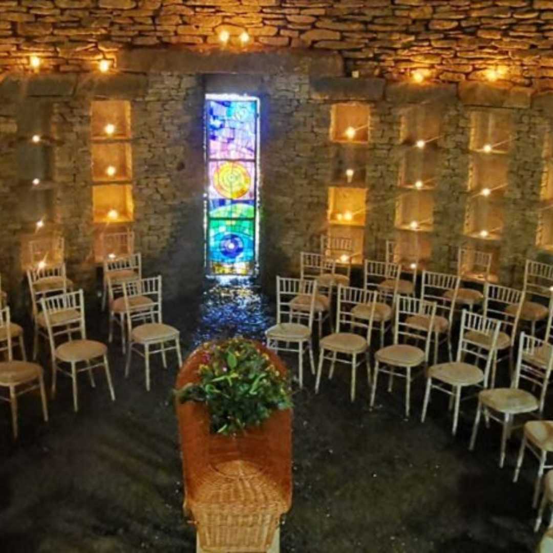 A curved formation of chairs around a coffin with votive candles in niches in the walls.